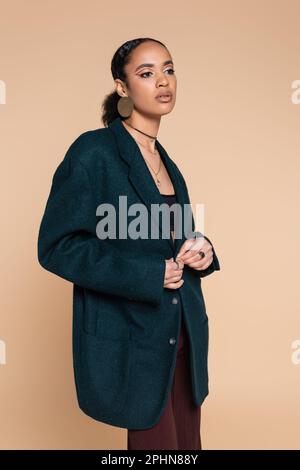Elegantes afroamerikanisches Modell in dunkelblauem Wollblazer, isoliert auf beige, Stockbild Stockfoto