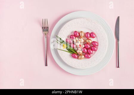 Frohe Ostern. Tischdecken für Osterferien. Ostereier, Kaninchen, Blumen und Besteck auf pinkfarbenem Hintergrund. Draufsicht, flach liegend Stockfoto