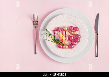 Frohe Ostern. Tischdecken für Osterferien. Ostereier, Ente, Blumen und Besteck auf pinkfarbenem Hintergrund. Draufsicht, flach liegend Stockfoto