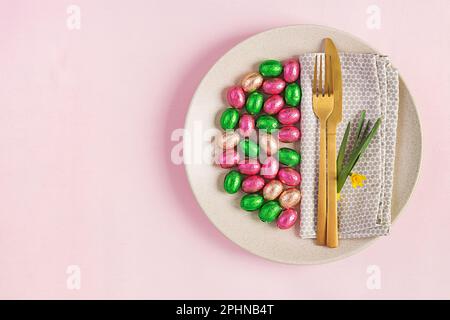 Frohe Ostern. Tischdecken für Osterferien. Ostereier, Blumen und Besteck auf pinkfarbenem Hintergrund. Draufsicht, flach liegend Stockfoto