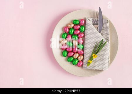 Frohe Ostern. Tischdecken für Osterferien. Ostereier, Blumen und Besteck auf pinkfarbenem Hintergrund. Draufsicht, flach liegend Stockfoto