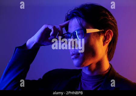 Porträt eines selbstbewussten jungen Mannes, der die Brille anpasst und wegschaut Stockfoto