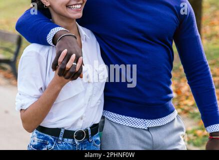 Interrassistische Liebe in Herbstglühen: Nahaufnahme von Black Boy und unbekanntem Weißen Mädchen, die inmitten von gefallenen Blättern im Sunset-lit Park umherschwirren Stockfoto