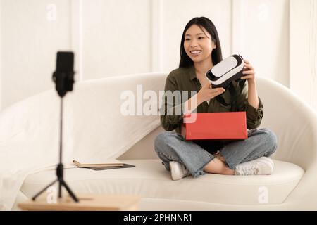 Asiatische Beeinflusserin eröffnet Paket und Streaming und zeigt VR-Headset Stockfoto