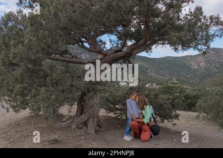 Mutter und Tochter in Sportbekleidung und mit Rucksäcken wandern durch den Wald und die Berge. Touristen kleben im Wacholdergesicht. Mutterliebe. Familienspaziergang in der Natur. Hochwertiges Foto Stockfoto