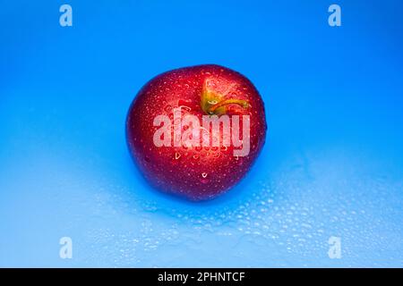 Die Wassertropfen auf dem roten Apfel auf blauem Hintergrund. 2023-03-17-23-56-23 Stockfoto