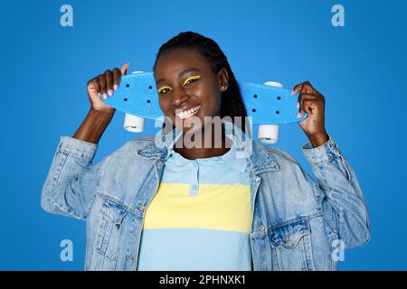Positiv-cool-stylische junge schwarze Frau mit Skateboard, Studioaufnahme Stockfoto