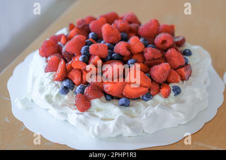 Großer Pavlova-Kuchen mit Erdbeeren, Blauberris und Himbeeren auf dem Tisch. Erdbeerparty Stockfoto