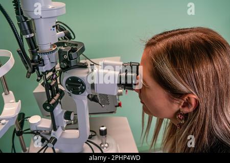 Junge Frau, die in die Augenuntersuchungsmaschine im Optometrien-Ambulanz schaut Stockfoto