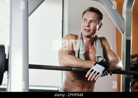 Verschwitzter, müder Sportler, der sich nach dem Training auf die Glocke lehnt Stockfoto