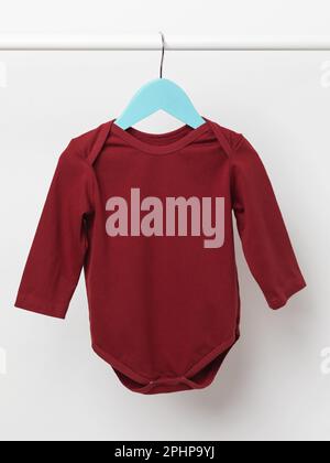 Kinderanzug mit langen Ärmeln an einem Kleiderbügel, burgunderfarbener Body für Kinder auf hellem Hintergrund Stockfoto