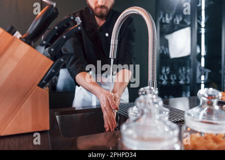 Professioneller junger Koch kocht in Uniform und wäscht die Hände an der Küche Stockfoto