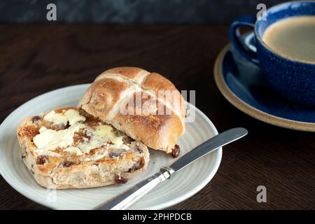 Ein Osterbrötchen mit heißem Kreuz, getoastet und serviert mit Butter, die auf dem warmen Brötchen schmilzt. Traditionell am Karfreitag in Großbritannien serviert Stockfoto