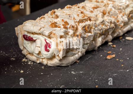 Der Konditor des Küchenchefs rollt die Baiser zu einer Rolle mit Beerenconfit und Creme Stockfoto