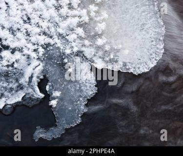 Eine malerische Winterszene eines gefrorenen schwedischen Flusses, der mit komplexen Eisformationen glitzert und von einer frostigen Schneeschicht überzogen ist. Stockfoto