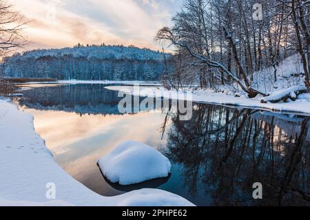 Eine Winterszene in Schweden mit einem ruhigen Fluss, der Bäume, Schnee und die Schönheit der Umgebung bei kalten Temperaturen reflektiert. Stockfoto