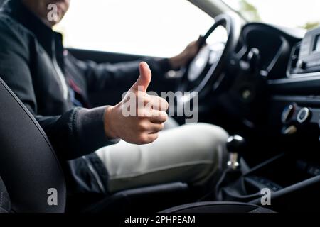 Glücklicher Fahrer im Auto, Daumen hoch. Mann am Steuer. Positiver Neuwagenkäufer und -Besitzer. Guter Kundenservice in Taxi, Autohaus, Versicherung. Stockfoto