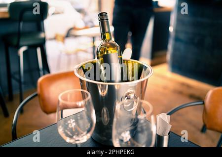 Eine Flasche Wein im Eiskübel auf dem Restaurant- oder Bartisch. Getränkekühler im Pub. White sauvignon Blanc, chardonnay oder riesling. Stockfoto