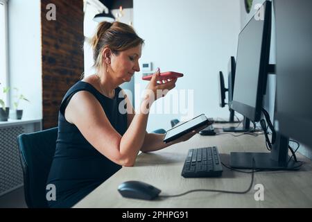 Geschäftsfrau mit Geschäftsanruf, die im Büro am Tablet arbeitet. Reife beschäftigte Frau mit Touchpad-Computer, der am Fenster in einem modernen Interieur steht. Fema Stockfoto