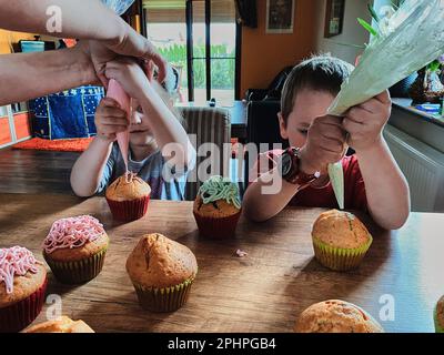 Gruppe von Kindern backen Cupcakes, Quetschen von Creme aus Süßwarenbeutel, Zubereitung von Zutaten, Belag, Streuseln für die Dekoration von Cookies. Kinder kochen Stockfoto