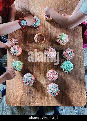 Gruppe von Kindern backen Cupcakes, Zutaten vorbereiten, Belag, Streuseln für die Dekoration Cookies. Kinder kochen, arbeiten zusammen in der Küche zu Hause Stockfoto