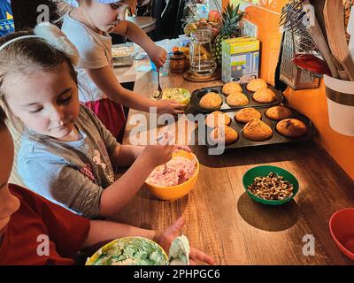 Gruppe von Kindern backen Cupcakes, Zutaten, Toppings, Streuseln für die Dekoration von Cookies. Kinder lernen zu kochen, arbeiten zusammen in Kitch Stockfoto