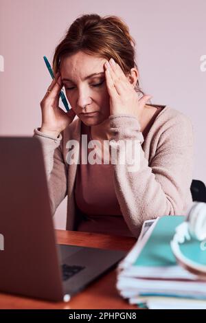 Frau konzentrierte sich auf ihre Arbeit und arbeitete hart, um ihre Arbeit von zu Hause aus auf einem Laptop zu erledigen. Frau, die am Schreibtisch vor dem Computer sitzt und auf den Bildschirm blickt Stockfoto