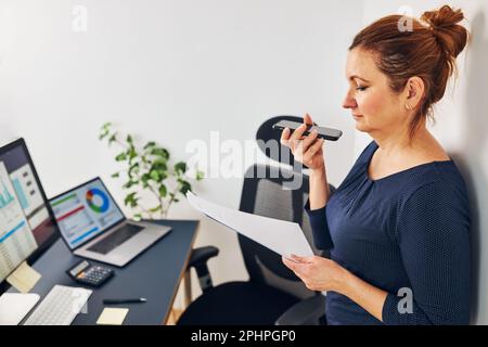 Unternehmerin, die ein Geschäftsgespräch mit dem Mobiltelefon führt. Geschäftsfrau, die im Büro arbeitet und Dokumente und ein Smartphone besitzt. Frau steht bereit Stockfoto