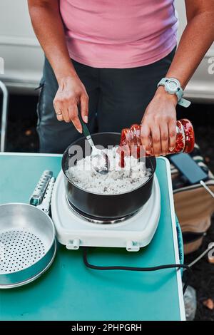 Nahaufnahme von weiblichen Händen, die Tomatensauce in Reisschale geben. Frau kocht Essen auf Elektroherd auf Camping während der Sommerferien. Camping-Leben, Pre Stockfoto