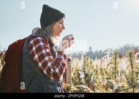 Frau macht Pause und entspannt sich mit einer Tasse Kaffee während der Sommerreise. Eine Frau, die auf der Spur steht und wegschaut. Frau mit Rucksack, die durch Ta wandert Stockfoto