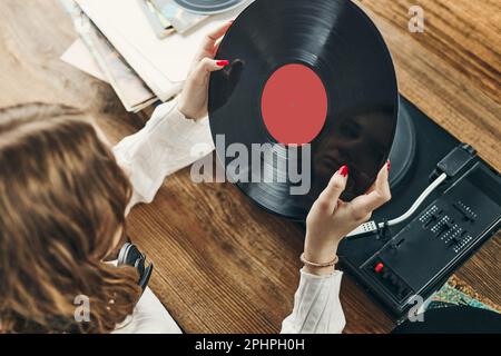 Junge Frau, die Musik von einem Plattenspieler hört. Wiedergabe von Musik auf Plattenspielern. Frau, die zu Hause Musik aus der alten Plattensammlung genießt. Stockfoto