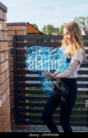 Junge Frau wirft leere gebrauchte Plastikwasserflaschen in den Abfalleimer. Sammeln von Kunststoffabfällen zum Recycling. Konzept der Plastikverschmutzung und auch Stockfoto