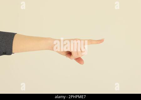 Die Hand einer Frau zeigt mit dem Zeigefinger auf einen beigen Hintergrund Stockfoto