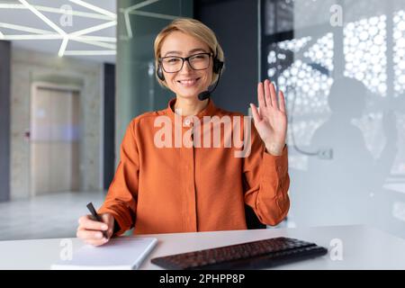 Online lernen. Porträt einer jungen Schülerin, Lehrerin mit Headset, die im Büro am Tisch sitzt und in einem Videogespräch mit der Kamera spricht. Lernt, lehrt. Stockfoto