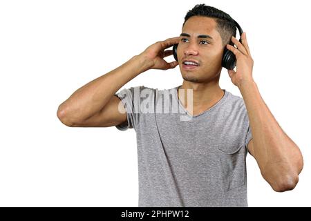 Der 28-jährige Brasilianer hält mit beiden Händen kabellose Kopfhörer, hört Musik und blickt auf den Horizont. Stockfoto