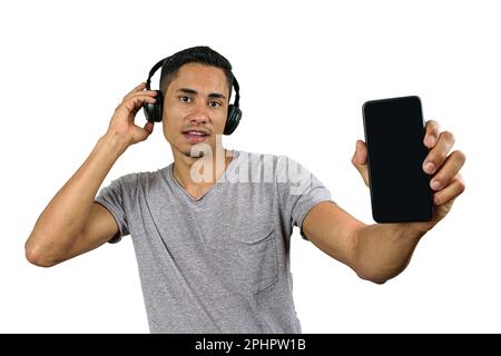 Der 28-jährige Brasilianer mit einem überraschten Gesicht, mit einer Hand auf dem kabellosen Kopfhörer, zeigt das Smartphone der Kamera. Stockfoto