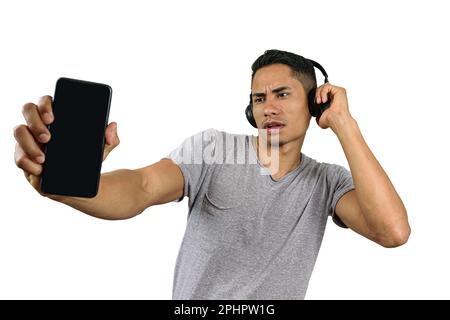 Der 28-jährige Brasilianer mit einer Hand auf dem kabellosen Kopfhörer schaute auf sein Smartphone und zeigte es der Kamera. Stockfoto