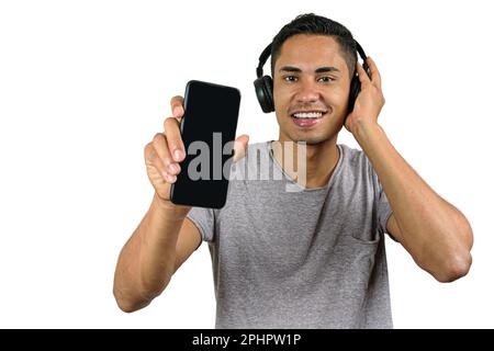 Lächelnder 28-jähriger Brasilianer mit einer Hand auf dem kabellosen Kopfhörer und der anderen zeigt sein Smartphone der Kamera. Stockfoto
