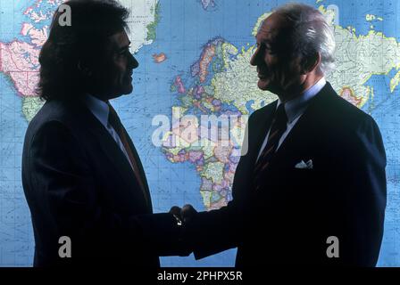 1990 HISTORISCHE SILHOUETTE MÄNNLICHE BÜROANGESTELLTE HANDSCHLAG AUF DER WELTKARTE („RAND MCNALLY 1990“) Stockfoto