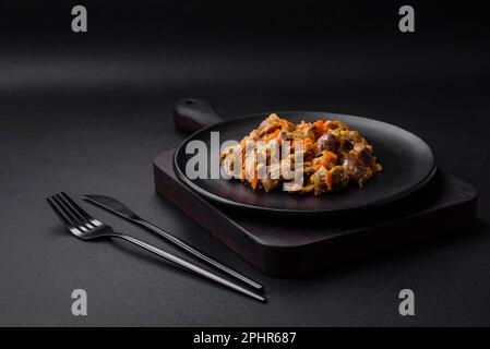 Köstliche gedünstete Hühnermagen mit Karotten und Tomaten auf dunklem Betonhintergrund Stockfoto