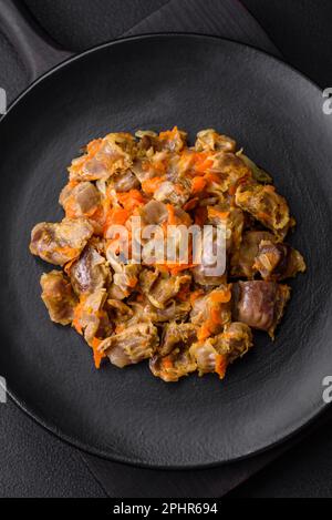 Köstliche gedünstete Hühnermagen mit Karotten und Tomaten auf dunklem Betonhintergrund Stockfoto