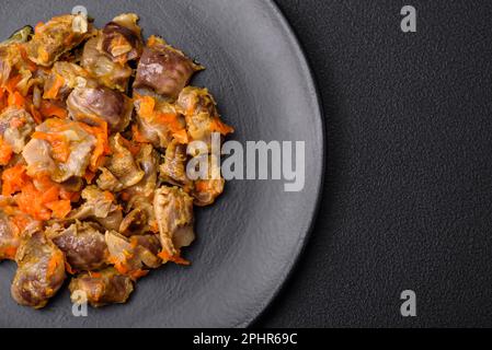 Köstliche gedünstete Hühnermagen mit Karotten und Tomaten auf dunklem Betonhintergrund Stockfoto