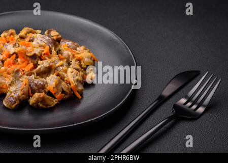 Köstliche gedünstete Hühnermagen mit Karotten und Tomaten auf dunklem Betonhintergrund Stockfoto