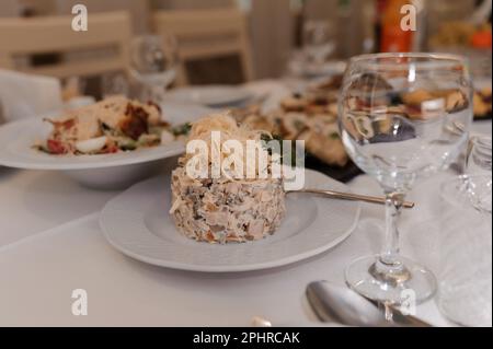 Salat mit Käse, Tomaten und Ei auf einem weißen Teller. Salat auf dem Feiertagstisch Stockfoto