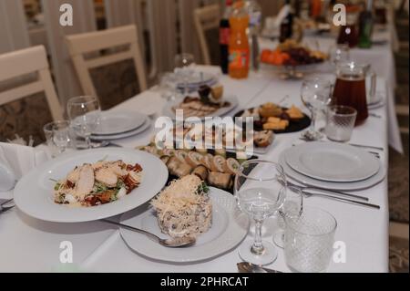 Salat mit Käse, Tomaten und Ei auf einem weißen Teller. Salat auf dem Feiertagstisch Stockfoto