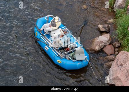 Zwei Männer sitzen in einem blauen Schlauchboot mit Angelausrüstung am Ufer des Roaring Fork River, Carbondale, Colorado, USA. Stockfoto