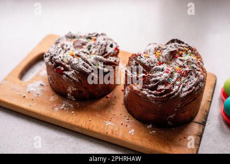 Osterkraffin auf hellem Holzhintergrund. Kuchen mit kandierten Früchten, Rosinen, Schokolade, Nüssen, Garnierung mit Puderzucker, essbare Dekorationen. Rustikal Stockfoto