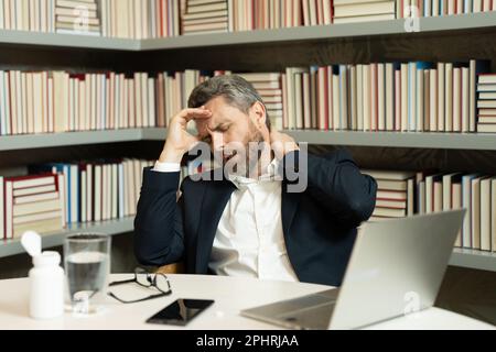 Der Millennials-Geschäftsmann im Büro hat Kopfschmerzen. Geschäftsmann im Anzug arbeitet mit einem Notebook im Heimbüro und nimmt die Brille ab. Er leidet unter Migräne oder Kopfschmerzen Stockfoto