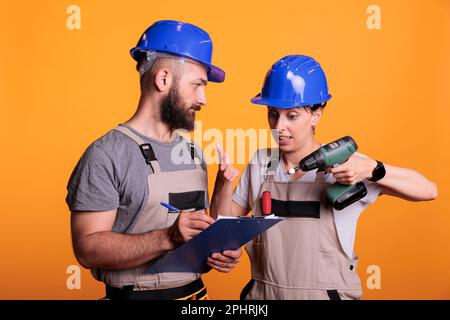 Ingenieure untersuchen Konstruktionsmessungen auf Klemmbrettern, halten Papier und Bohrpistole. Fremdfirmen sprechen über Renovierungsprojekte und bereiten sich auf Renovierungsarbeiten vor. Stockfoto
