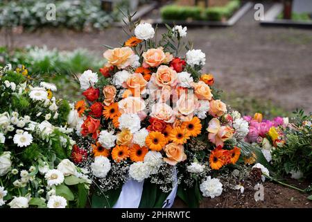 Stilvolle Bestattungsblumen mit weißen Nelken, orangefarbener Gerbera und roten und rosa Rosen auf einem Grab nach einer Beerdigung Stockfoto